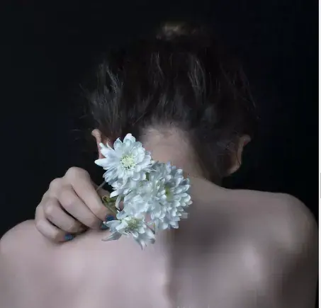 Back view of a bare-shouldered woman holding white chrysanthemums against her neck, used for All of Zen institut in Paris