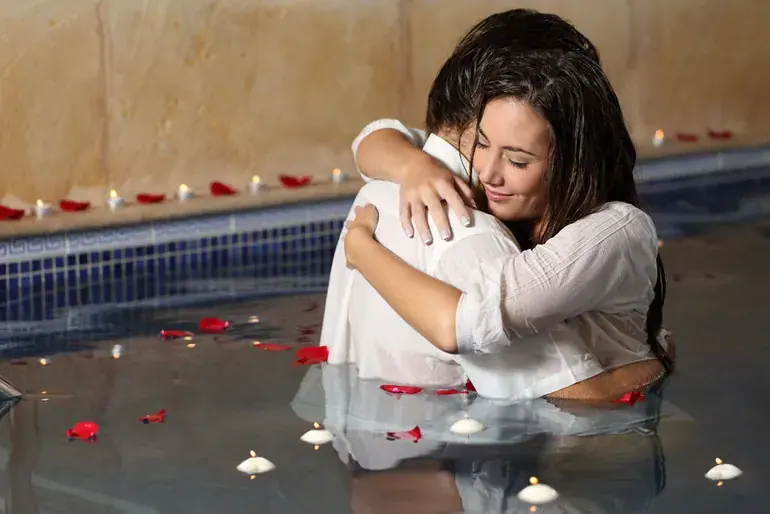 Couple embracing in a candlelit pool strewn with red rose petals, used for Anahata tantra massage salon in Warsaw