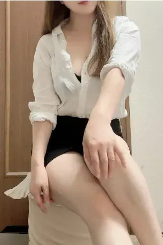 A woman in a white shirt and black skirt sits with her legs crossed, photographed for Analisamassage in Bangkok