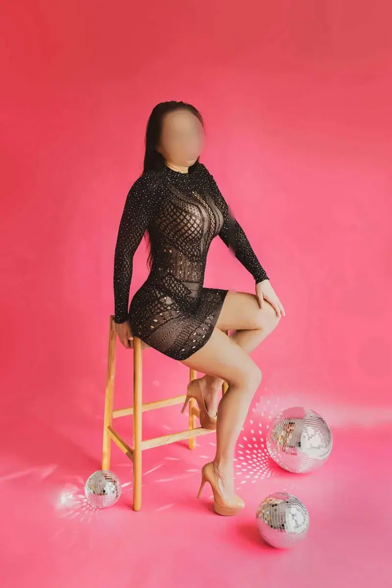 A woman with a blurred face poses on a wooden stool in a black lace dress beside disco balls at Angelhands Spa, Berlin