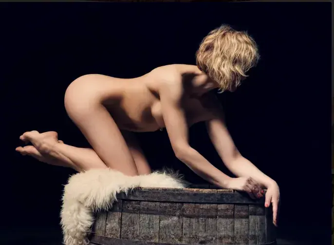 Artistic studio photo of a nude person with short blond hair kneeling on a wooden barrel, for Aphrodite Massages, Berlin