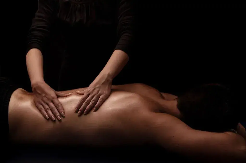 A masseuse's hands working on a person's bare back in dim light at ARTMASSAGE.HU, a massage salon in Budapest