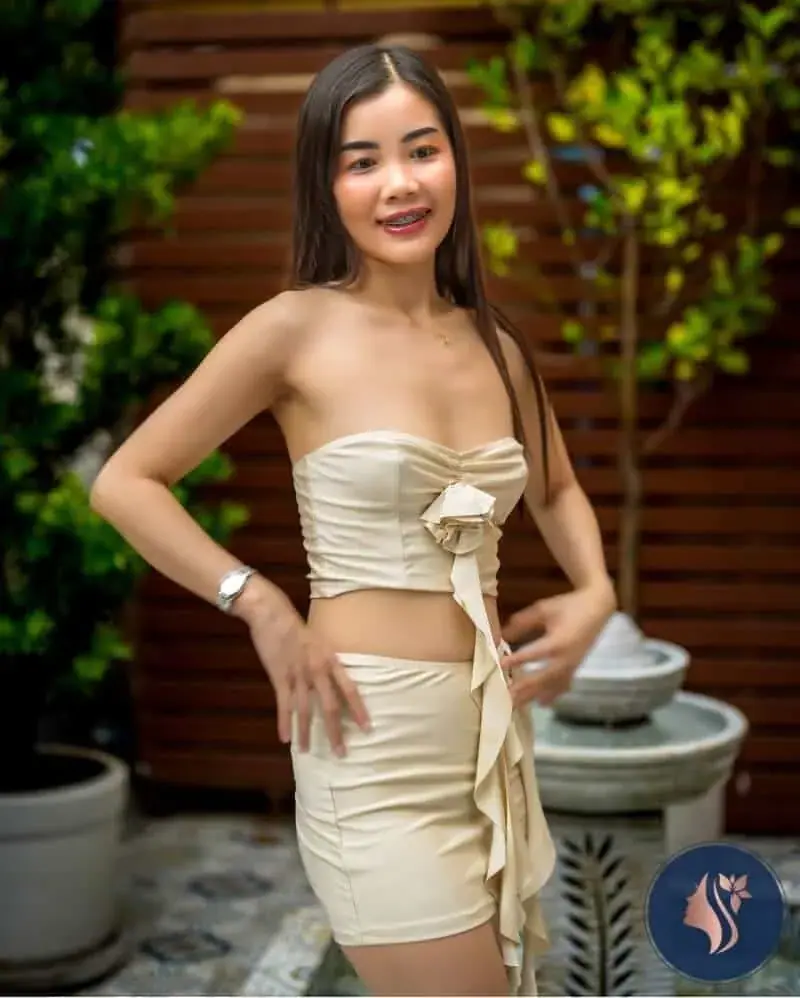 A smiling woman in a cream strapless top and skirt posing beside a small fountain at Aya Massage Bangkok
