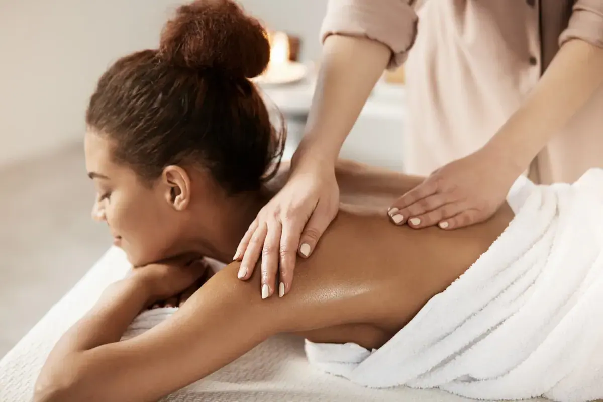 A woman lies relaxed on a massage table while a therapist massages her shoulders at Bain des Sens Spa, Paris
