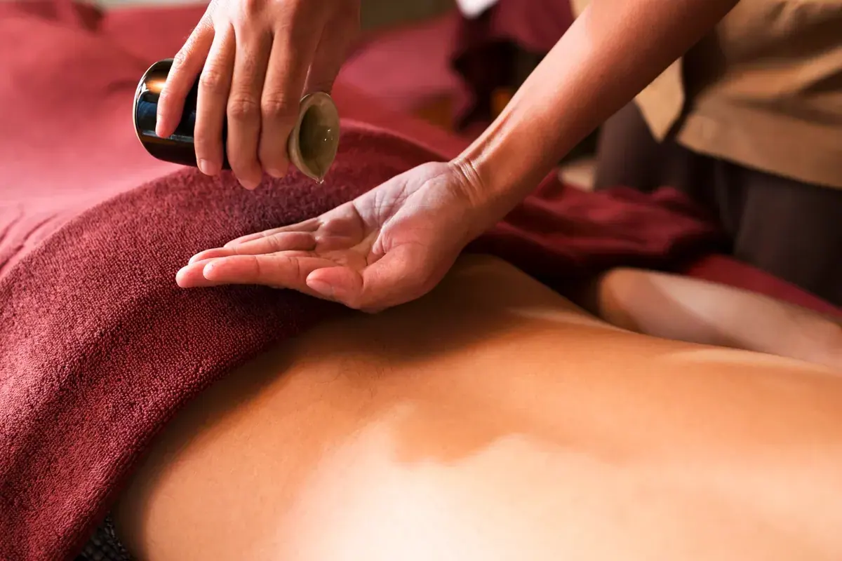 A therapist pours massage oil into her palm above a person's bare back at Bain des Sens Spa in Paris