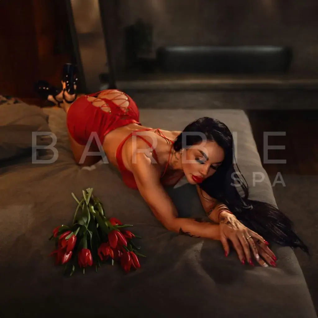 Woman in red lingerie and heels lying on a bed beside red tulips at Barbi Spa, Moscow