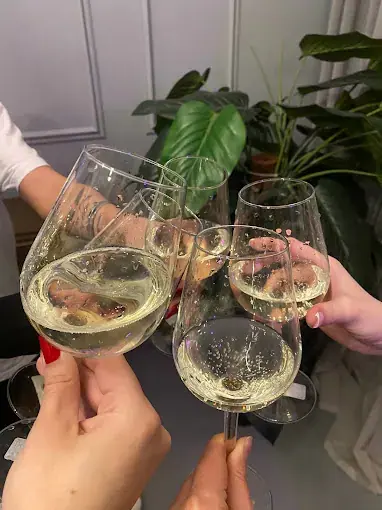 Guests clinking glasses of white wine in a toast at Black Velvet, Bucharest, with green plants in the background