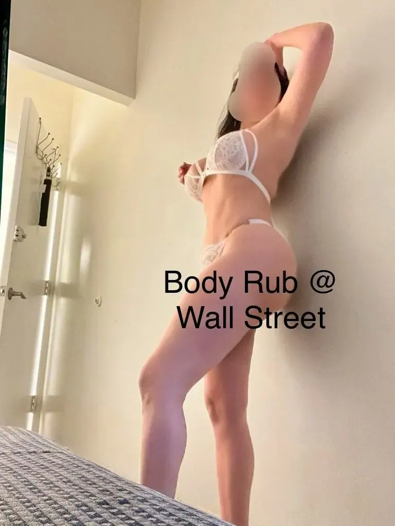 A woman in white lace lingerie posing against a wall in a bedroom, promoting Bodyrub at Wallstreet in New York
