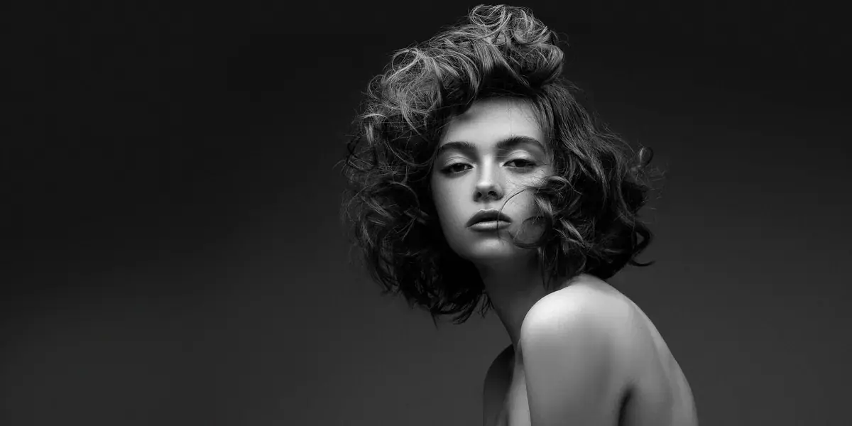 Black-and-white portrait of a young woman with voluminous curly hair looking at the camera, used for Czech Massage Sydney