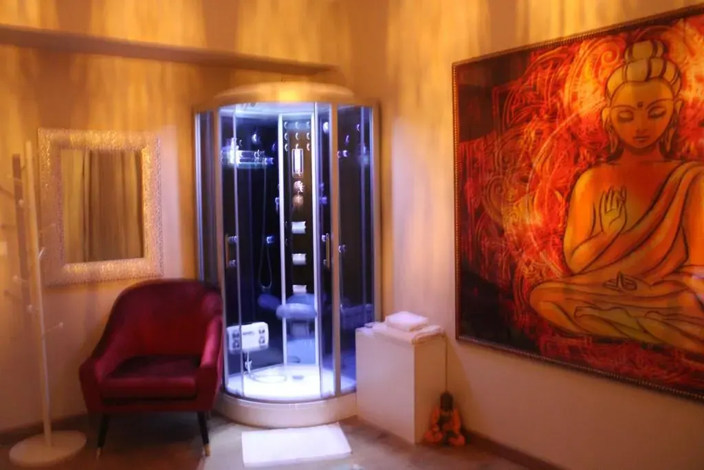 Warmly lit room at Delirio Spa in Lisbon with a steam shower cabin, red armchair and a large Buddha painting