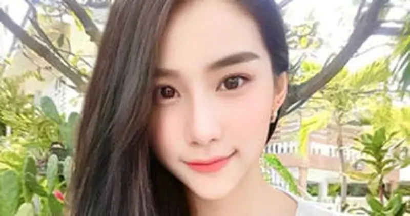 Close-up selfie of a smiling young woman with long dark hair outdoors among tropical plants, for Don Quixote Nuru Massage