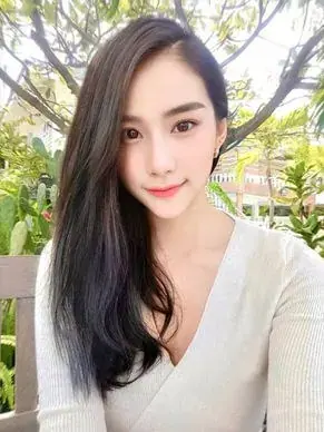 A smiling woman with long dark hair in a cream wrap top sits outdoors among green plants, a portrait for Don Quixote Nuru
