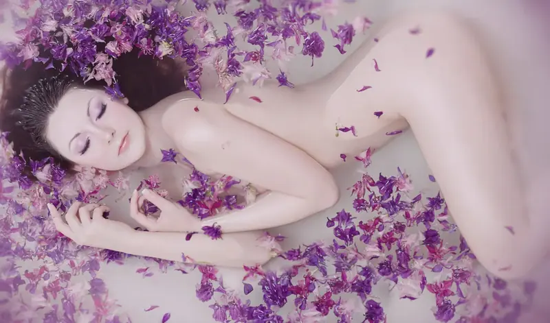 Woman lying in a bath covered in purple flower petals at Dream Girl Massage in Sydney