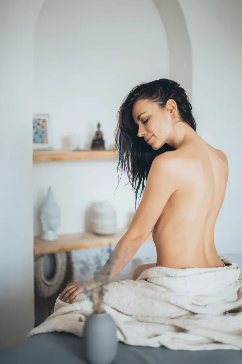 Woman with wet dark hair seated on a massage table wrapped in a towel, in a bright spa room at Eros Spa, Bucharest