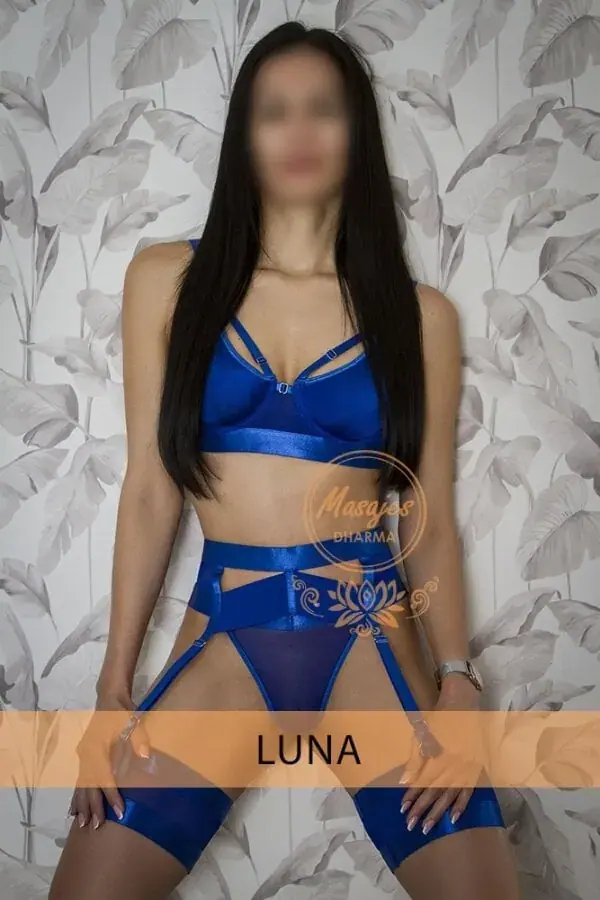 Woman with long dark hair posing in blue lingerie against a leaf-patterned wall at Erotic masajes dharma, Barcelona