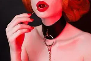 Close-up of a red-haired woman in a black leather collar with a metal ring and chain, in red lighting, Erotic Massage