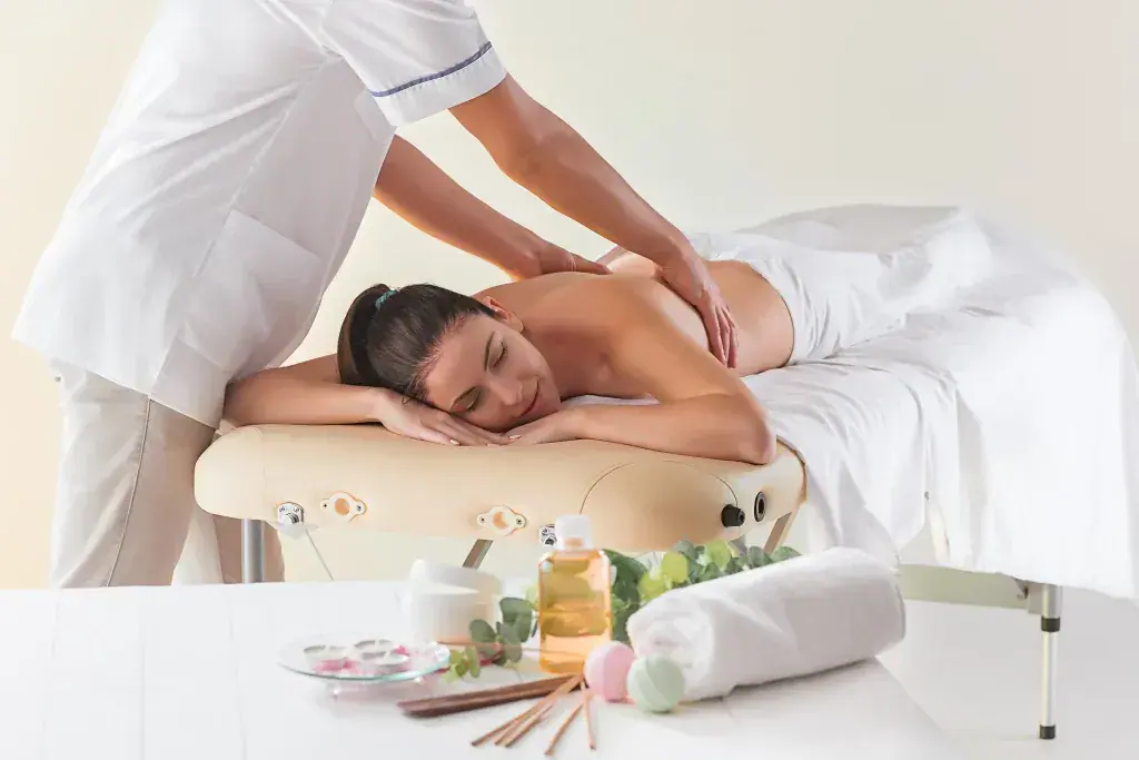 A therapist in white massages the back of a woman lying on a treatment table at Erotic Massage UK in London