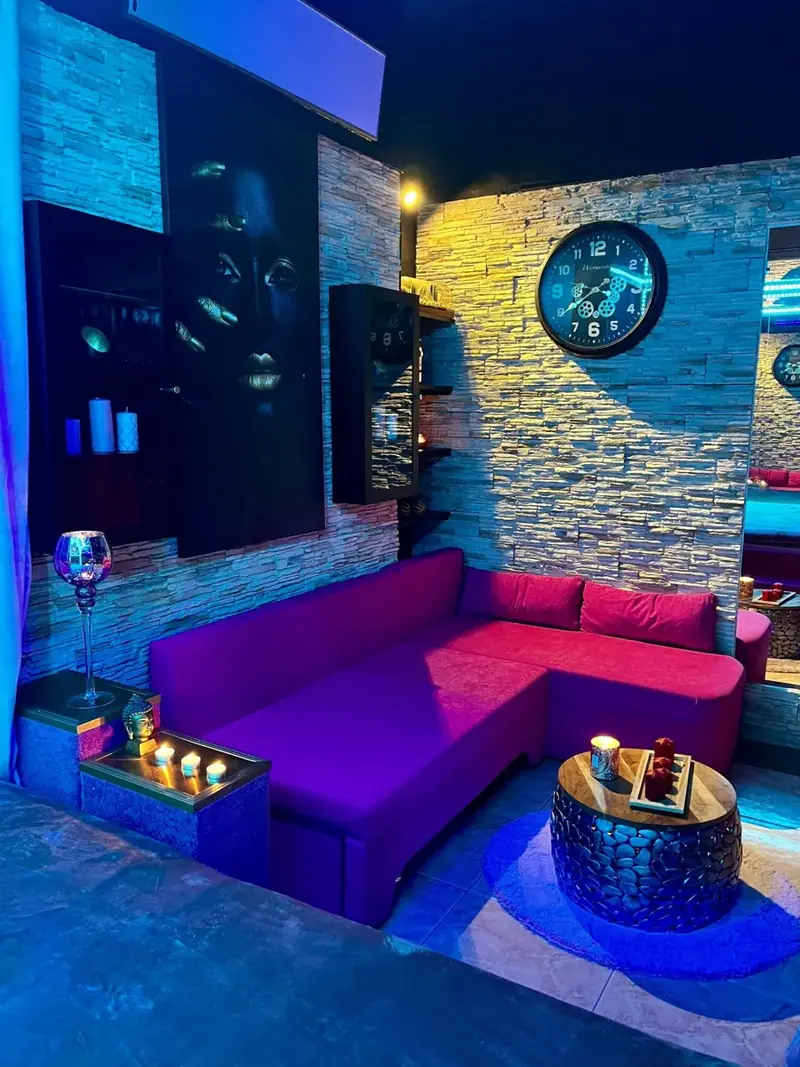 Lounge at Erotic Massages BRNO in Brno with a magenta corner sofa, stone walls, candles and a round wall clock