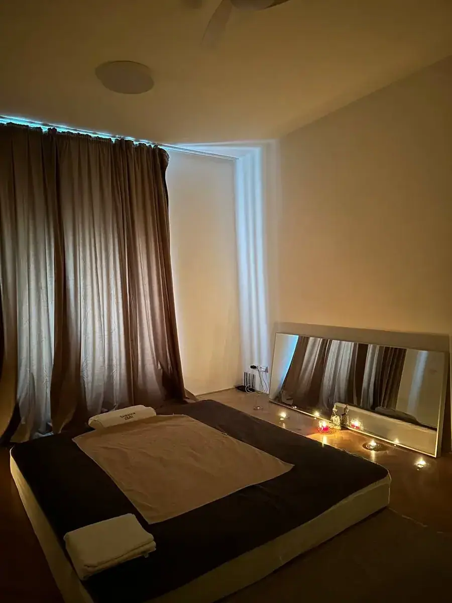 Dimly lit massage room with a low padded mat, folded towels, floor mirror and candles at Relax Massage in Brno