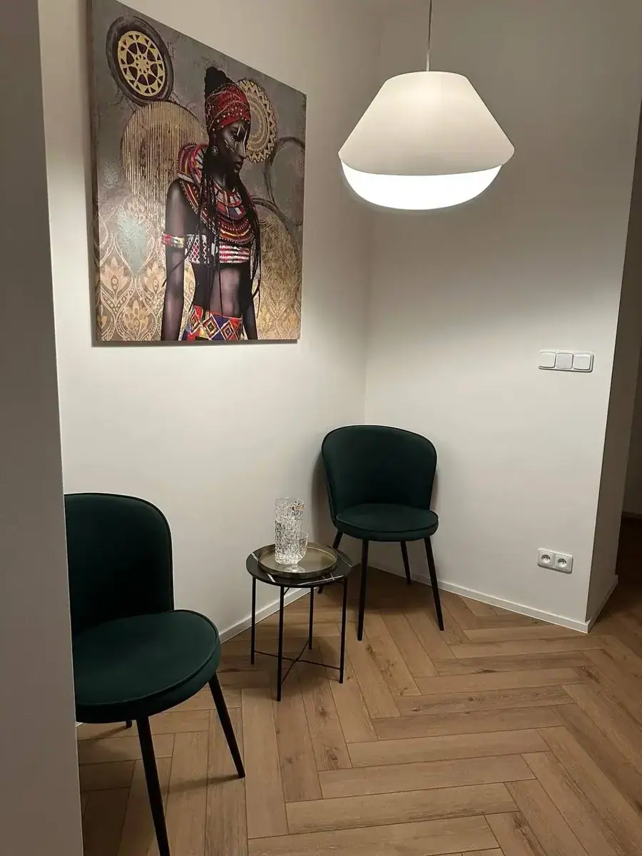 Waiting area at Erotické masáže Brno Relax Massage with two green chairs, a small side table and African-style wall art