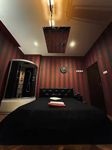 Dimly lit room with red striped walls, a large black bed and a glass shower cabin at Fantasy Masaj in Bucharest