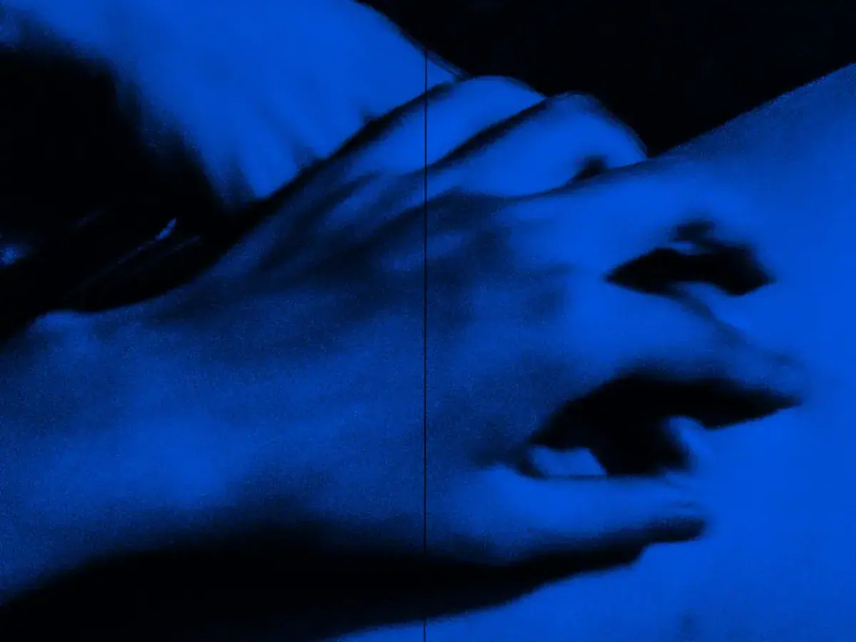 Close-up of a hand resting on skin in dark blue light, from Fantazie RAJSKE POTESENI massage salon in Prague