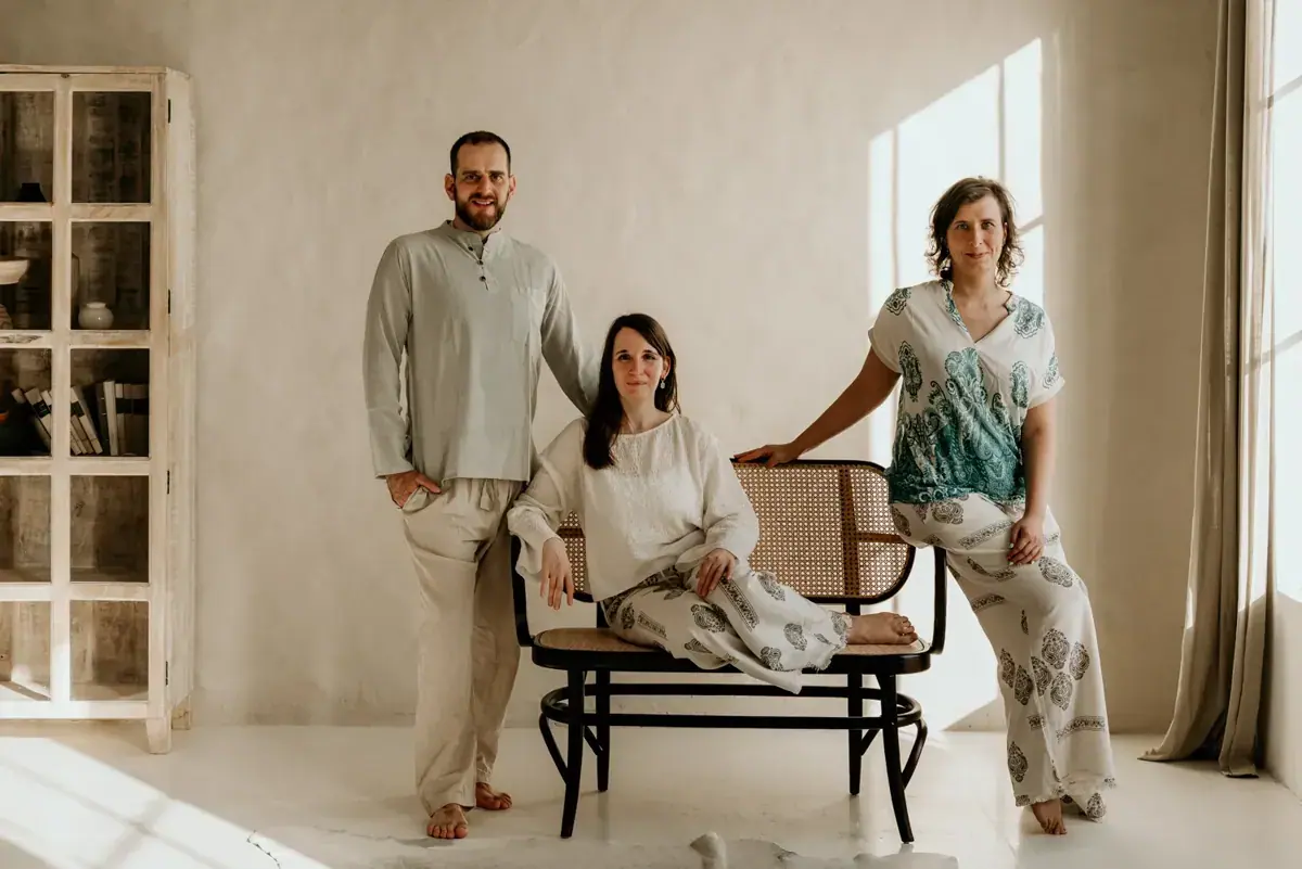 Three people in relaxed linen clothing pose around a cane bench in a bright, minimalist room at Gaia Szalon in Budapest