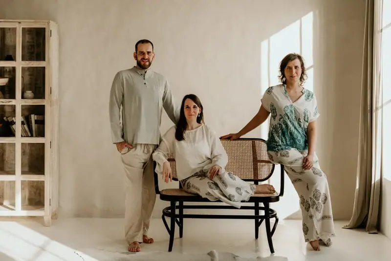 Three people in relaxed linen clothing pose around a cane bench in a bright, minimalist room at Gaia Szalon in Budapest