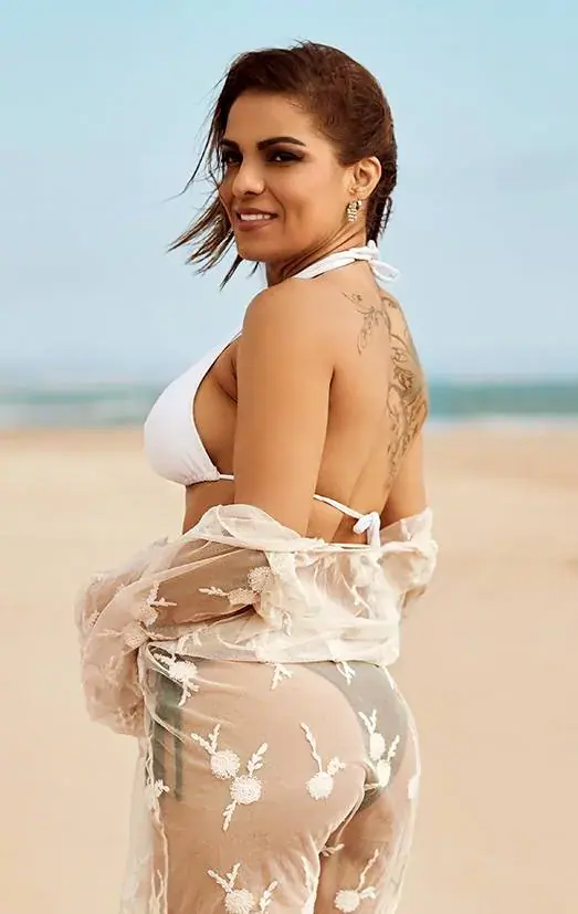 Smiling woman in a white bikini and sheer lace cover-up looking over her shoulder on a sandy beach
