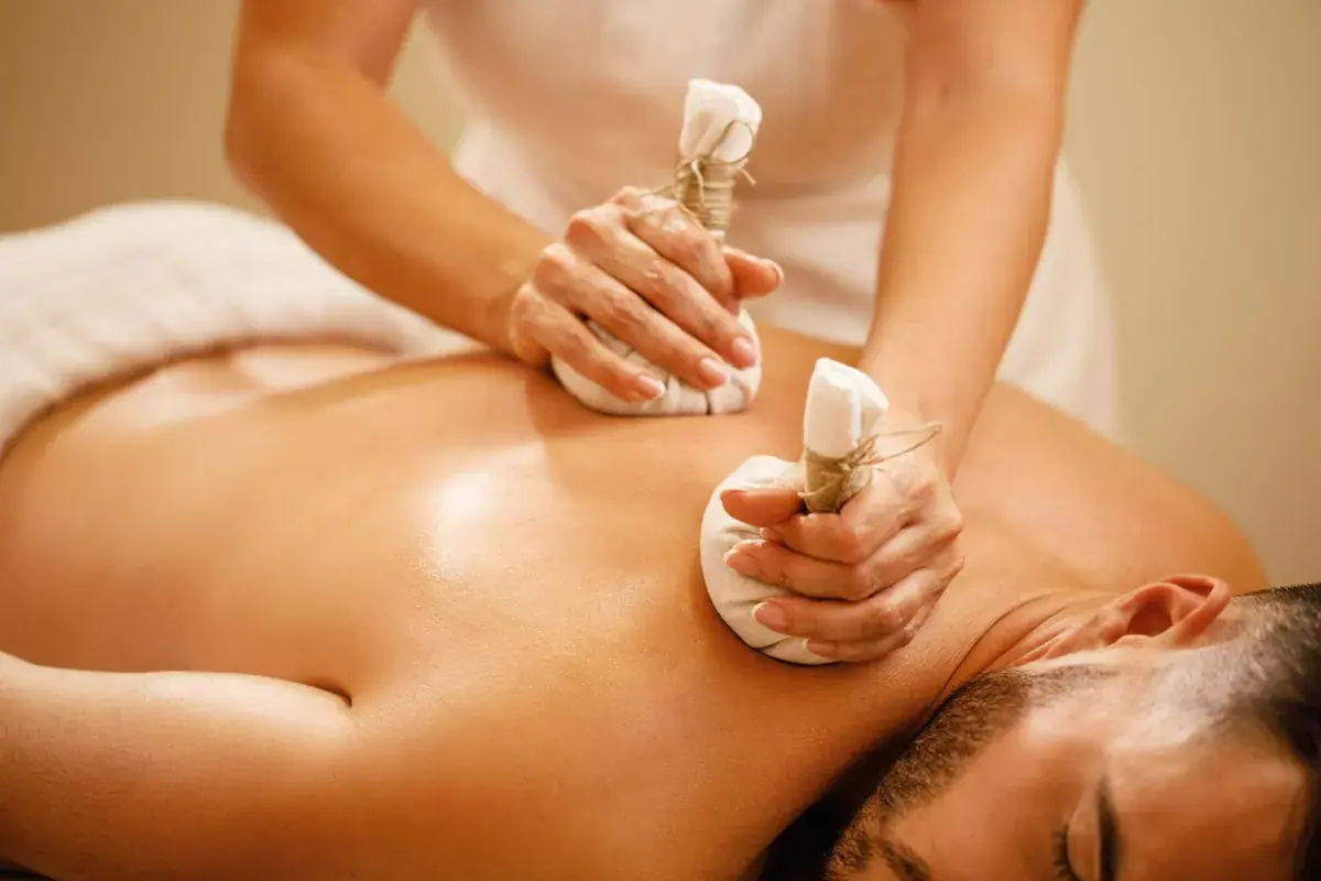 A therapist presses warm herbal compress bags onto a man's bare back during a massage at Go Kichi in Tokyo