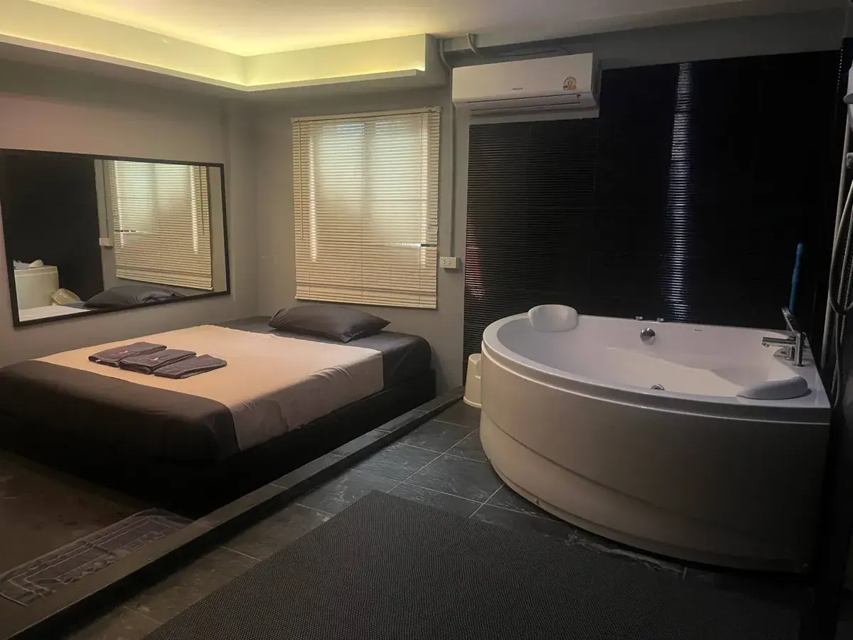 Dimly lit private room with a low bed, wall mirror and corner jacuzzi tub at Heal Nuru & Soapy Massage in Bangkok