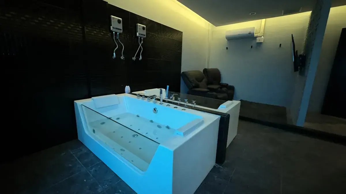 Dimly lit private room with two glass-fronted whirlpool tubs and a recliner chair at Heal Nuru & Soapy Massage in Bangkok