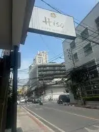 Street view of a corner building with a hanging sign for Hiso Nuru Massage on a sunny day in Bangkok