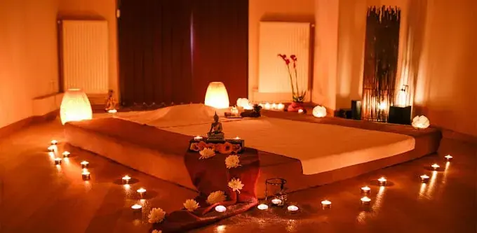 Candlelit massage room at iTantric in Bucharest with a low padded platform, a small Buddha statue and flowers