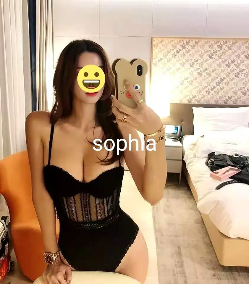 A woman in a black lace bodysuit takes a mirror selfie in a hotel-style bedroom, listed for Kent St Massage Sydney