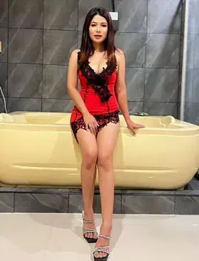 A masseuse in red dress posing by a bathtub at Kiss Bangkok Massage