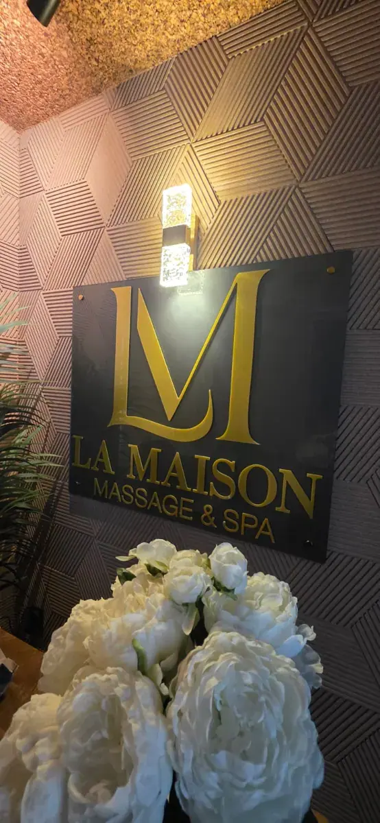 Gold lettered sign on a geometric paneled wall with white peony flowers in front, at La Maison Spa Baixa-Chiado in Lisbon