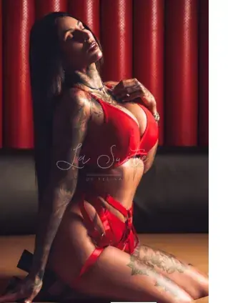 Tattooed woman in red lingerie kneeling against a red padded wall at la suitebcn Luxury Erotic in Barcelona