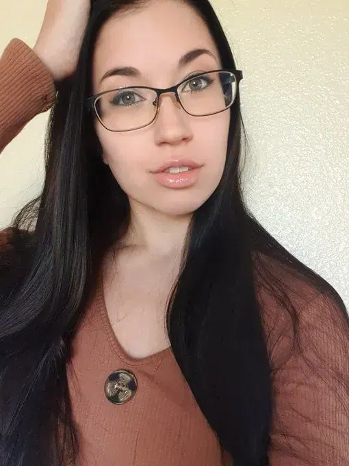 Selfie-style portrait of a woman with long dark hair and glasses, wearing a rust-colored top, for Leilalovesexy in Prague