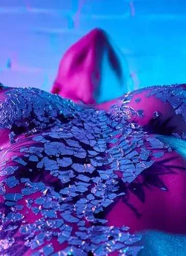 Artistic close-up of a body covered in shards of broken mirror glass under pink and blue light at Like Dream, Moscow