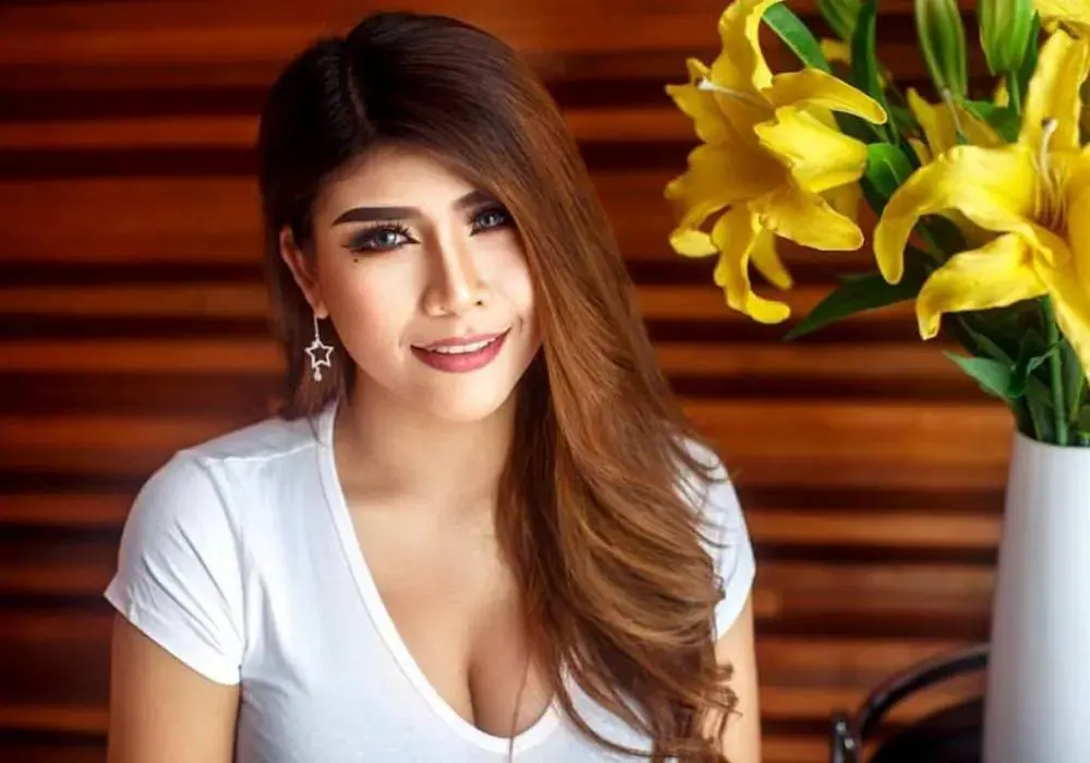Smiling woman with long brown hair in a white top beside yellow lilies, at Luxor Spa Sanpada in Mumbai