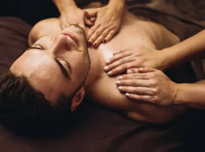 A shirtless man lies with closed eyes while a therapist's hands massage his chest at Majestique Tantra Massage in Bucharest