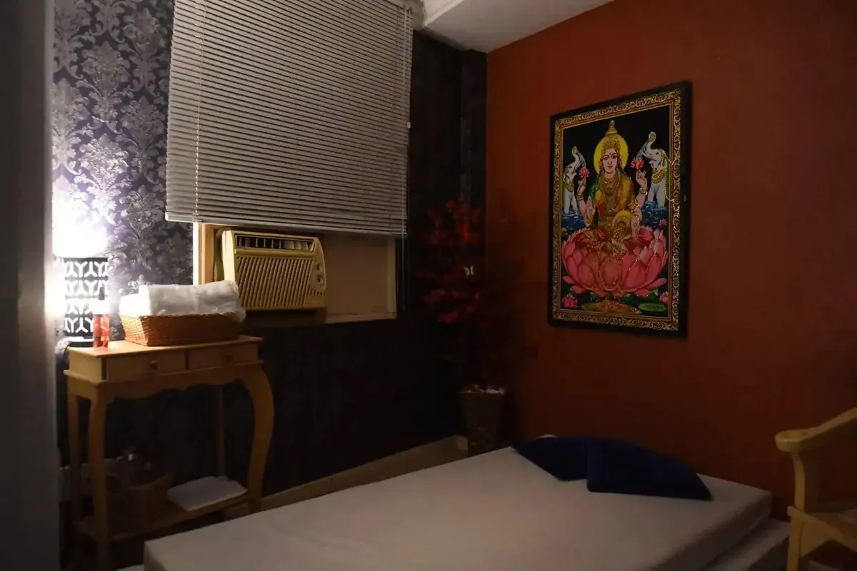 Dimly lit treatment room at Mandala Tantra RJ in Rio de Janeiro with a massage table, a small wooden console and a framed