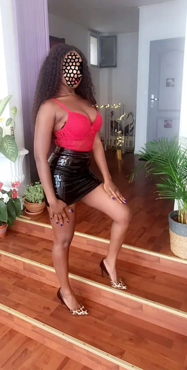 A woman in a red top, black vinyl skirt and leopard-print heels posing on wooden steps at Massage nuru Levallois, Paris