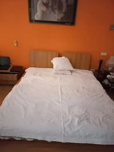 Double bed with white linens and a wooden headboard against an orange wall at Massage studio "FEMDOM" in Kyiv