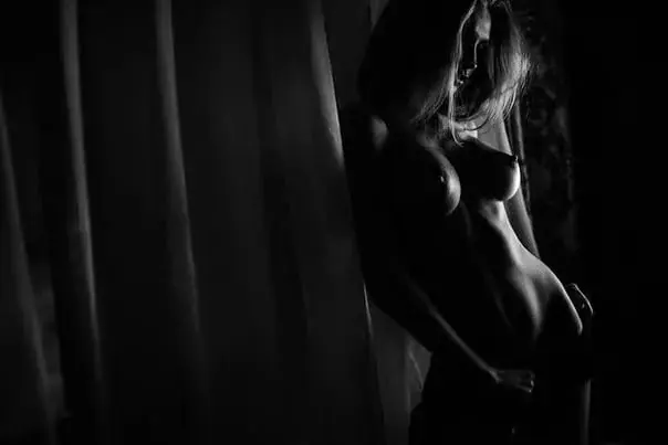 Black-and-white silhouette of a woman standing beside a curtain in low light, Massage212 erotic massage salon, New York