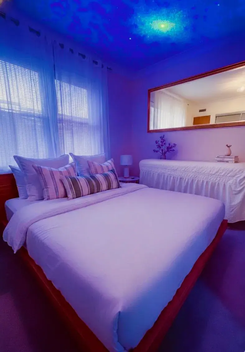 Bedroom at Mel Terapy in London with a made bed, striped cushions, a large mirror and a blue starry ceiling glow
