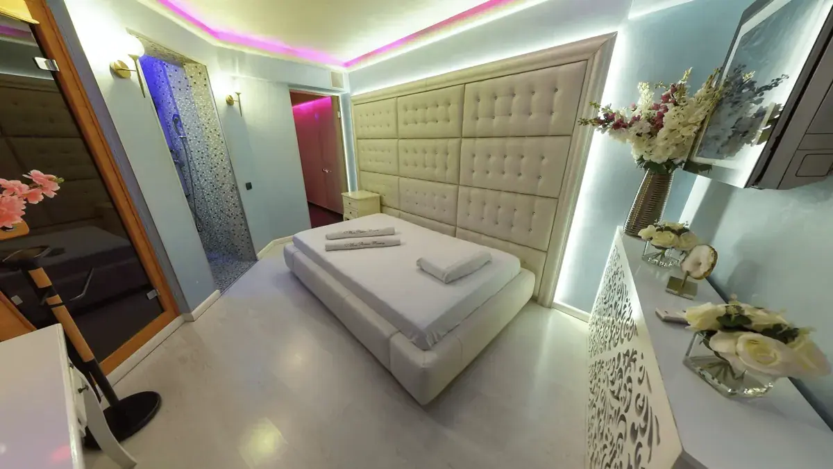 Treatment room at Mon Amour in Bucharest with a double bed, padded cream headboard and pink and white accent lighting