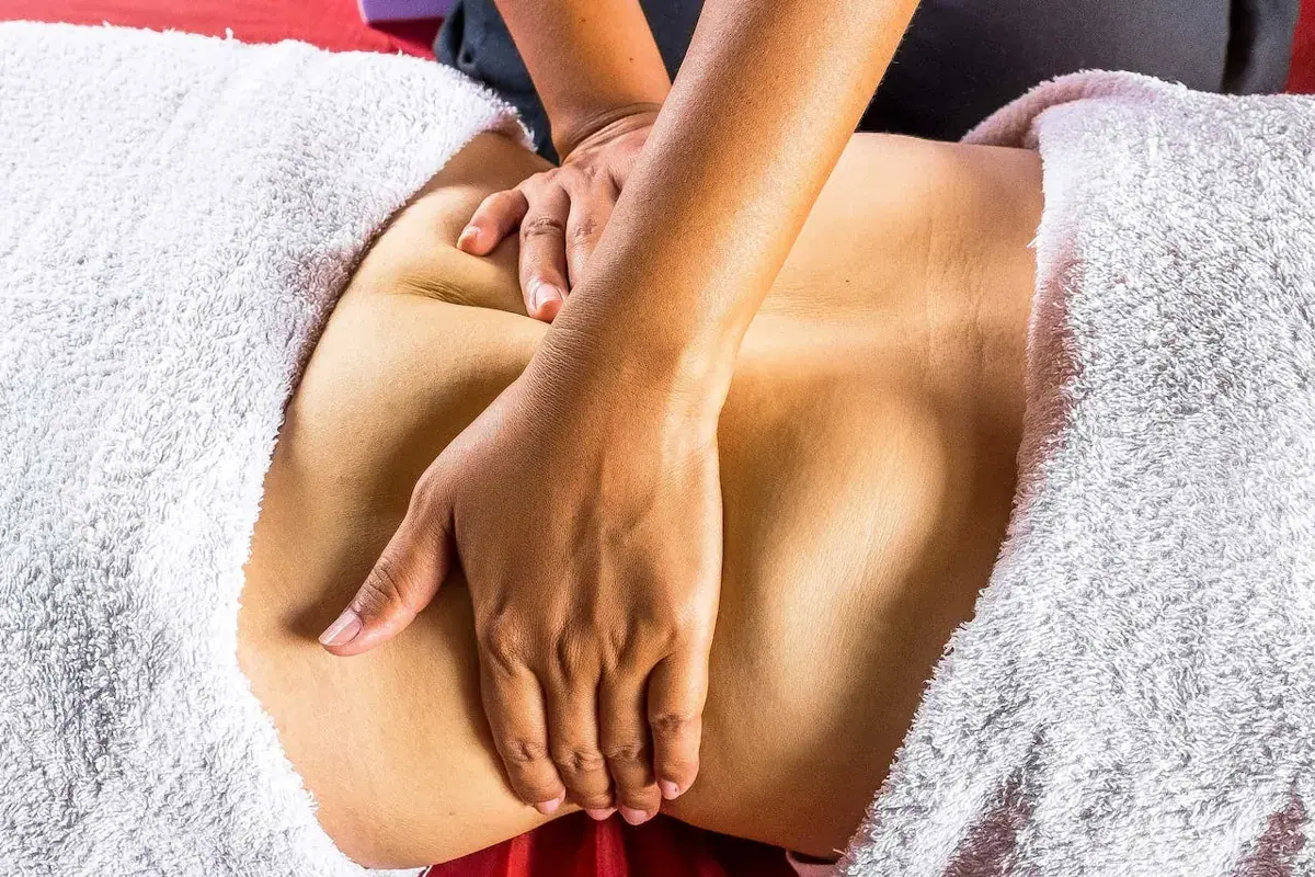 A masseuse's hands performing an abdominal massage on a client covered with white towels, at Mumbai Massage Services in