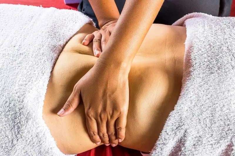 A masseuse's hands performing an abdominal massage on a client covered with white towels, at Mumbai Massage Services in
